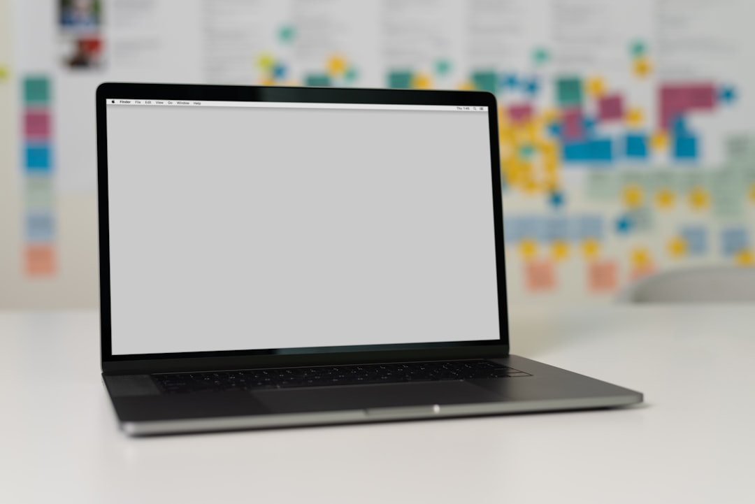 A laptop on a desk with an empty screen and colorful sticky notes in the background